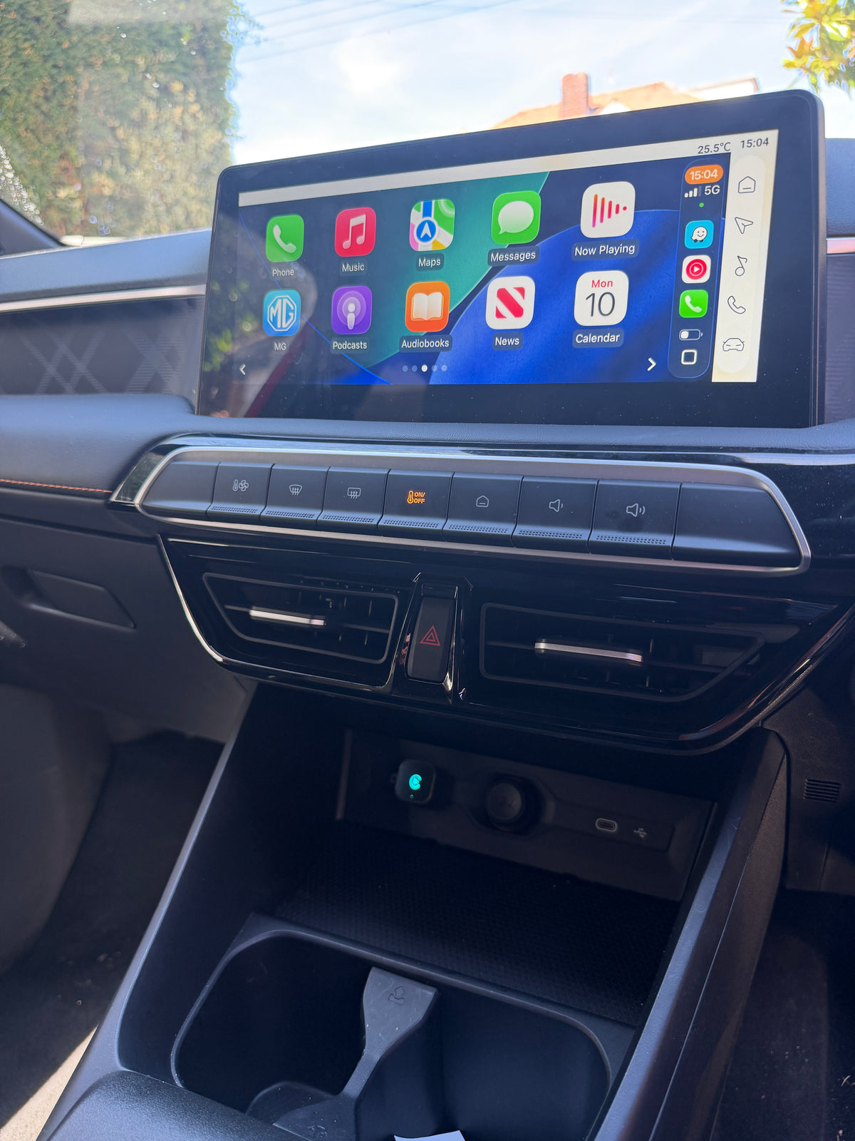 A car interior dashboard with a large touchscreen display showing Apple CarPlay interface, mounted above climate controls and a center console storage compartment.